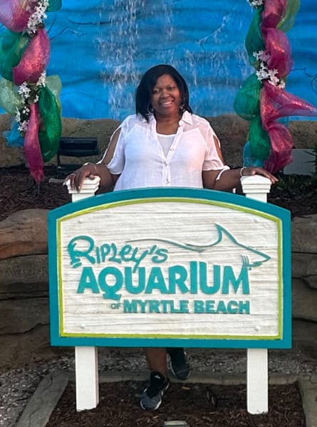 woman in a white top in front of an aquarium sign